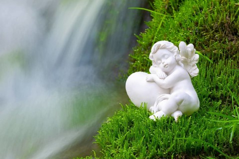 Porcelain angel figurine on moss by a waterfall