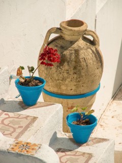 A large clay jug and two blue flower pots with plants adorn a rustic Mediterranean-style staircase,
