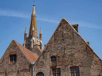 Old brick buildings with gothic tower in the background under a bright blue sky, historic city on