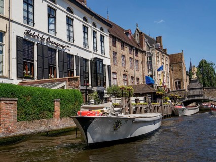 A hotel with a boat on a river, surrounded by historic buildings on a sunny day, historic city on