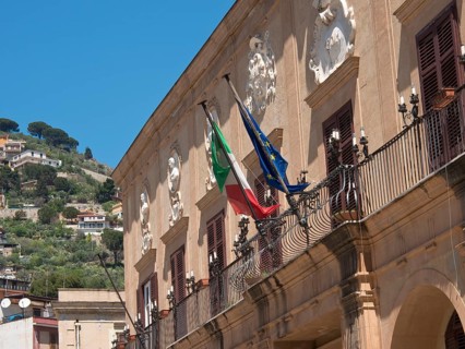 Building with italian and european flag on a balustrade in front of a sunny hillside, palermo in