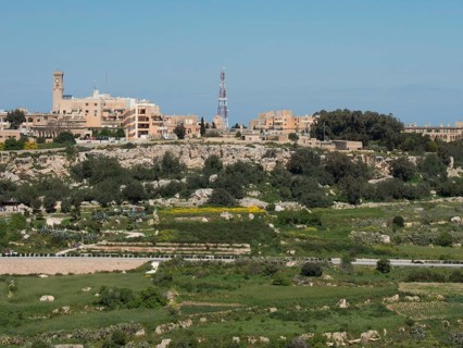Overview of a town with various buildings, green areas and a striking tower in the background, the