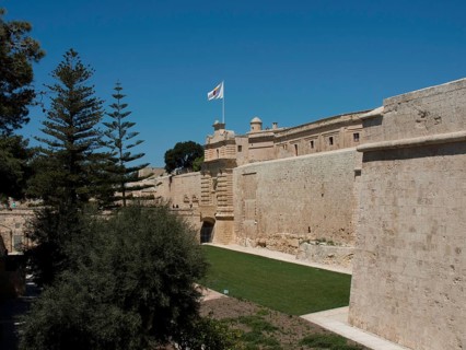 Historic fortress with protective stone walls, wide green spaces and a waving flag under a bright
