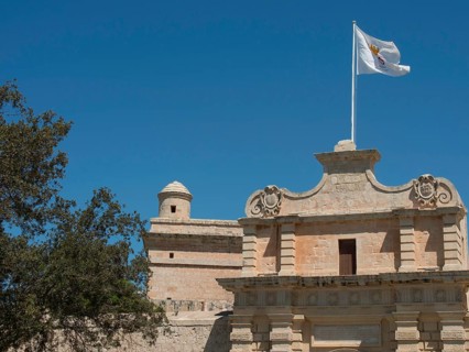 An old castle with a flag and a tower in the foreground, bright blue sky, historic buildings with