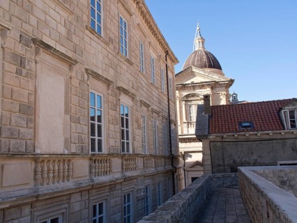 Old buildings with stone walls and many windows, in the background a dome under a blue sky, the old