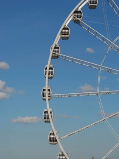 Partial view of a Ferris wheel with several cabins in front of a clear blue sky, the beach of