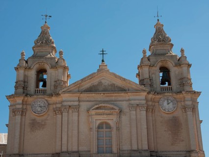 Front view of a historic church with two bell towers and clocks, the town of mdina on the island of