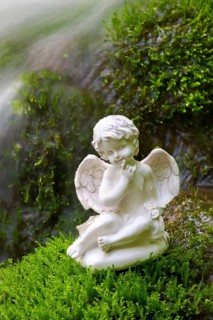 Porcelain angel figurine on moss by a waterfall