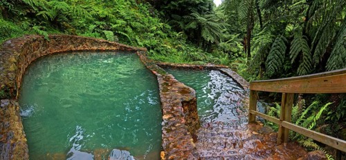Two turquoise-coloured thermal pools made of stone, surrounded by lush vegetation and ferns,