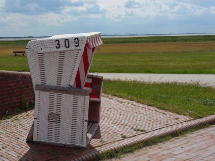 A white beach chair on the edge of a cobbled path with a view of a green meadow and the sea,