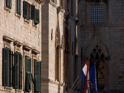 Detail of a historic stone facade with gothic style elements and flags in front of it, the old town