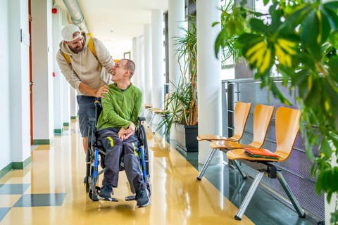 Disabled man with wheelchair and friend walking along in the university corridor
