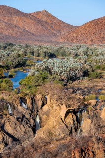Kunene River with green vegetation in dry red mountain landscape, waterfall and African Baobab