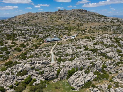 A rocky and dry landscape with two buildings under a cloudy sky, aerial view, karst mountains,