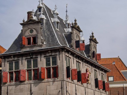 Historic building with red shutters, decorated roof and sculptures under a cloudy sky, historic