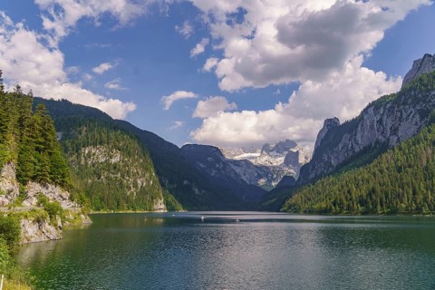 Majestic lake between high mountains and forests under a cloudy sky, turquoise green mountain lake