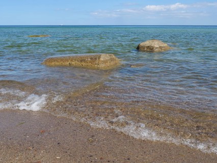 Clear sea water gently meets stones on the beach under a sunny, blue sky, spring on the Baltic Sea