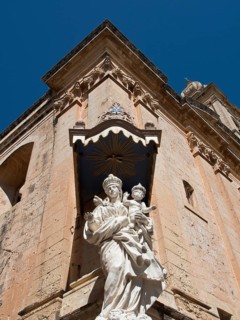 A statue of the holy mother and child in front of the corner of a historic building, the town of