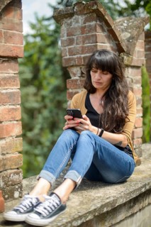 Young woman in casual clothing focused on conversation with smartphone in a peaceful garden with