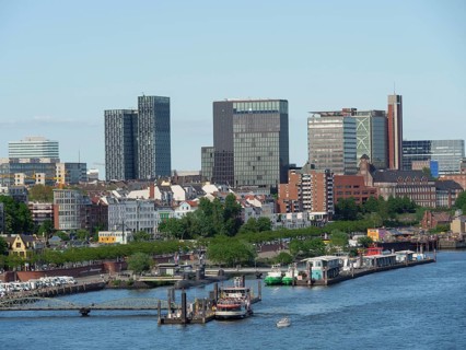 Modern skyscrapers and urban buildings on the riverside with boats and green areas under a clear