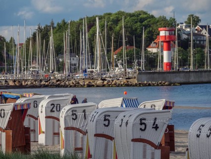 Holiday atmosphere at the coast with white beach chairs and a bright red and white lighthouse in