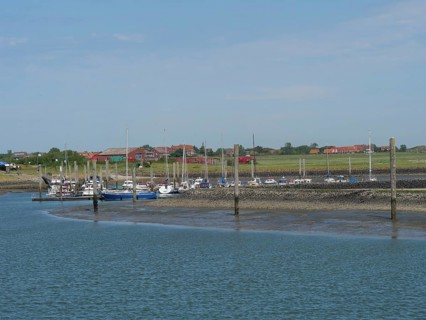 A village harbour with several boats moored, surrounded by the coastal landscape, Baltrum Germany