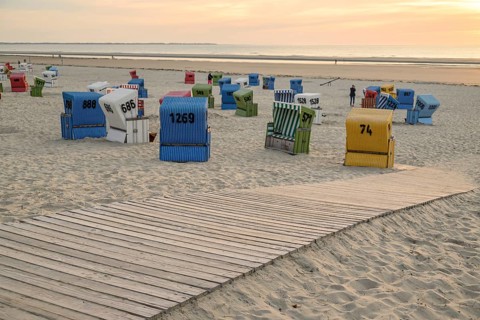 Colourful beach chairs on the sandy beach at sunset, a wooden path leads through the sand, summer