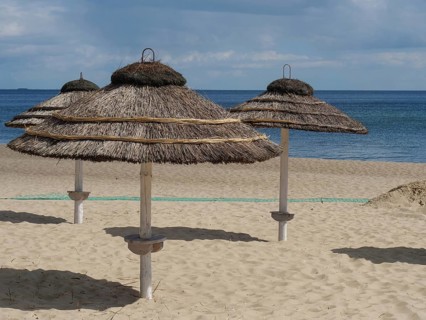 Beach with several thatched umbrellas and calm sea under partly cloudy sky, spring on the Polish