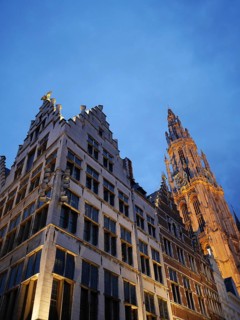 Gothic church tower and neighbouring buildings at dusk, illuminated against a dark blue sky, the