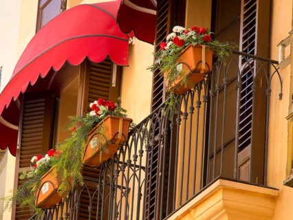 Decorative balcony with red awnings, flower pots and plants standing in front of windows of a