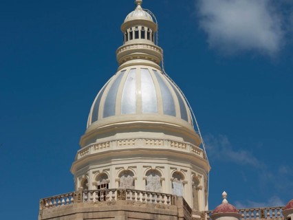 Large white-bluish dome of a religious building against a blue sky with some clouds, the island of