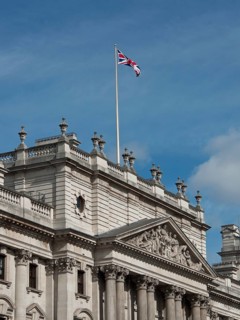 Historic building with a waving Union Jack flag on the roof, against a blue sky, London, England,