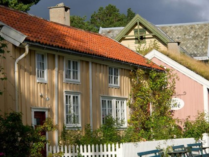 Yellow and pink house with a cafe sign and lush vegetation, colourful wooden houses behind white