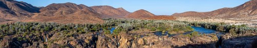 Panorama, Kunene River with green vegetation in dry red mountain landscape, waterfall and African