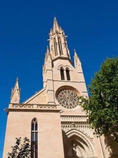 Gothic church facade with detailed rose window in front of a bright blue sky, palma de Majorca with