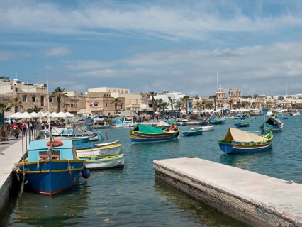 Several colourful boats in the harbour, surrounded by historic buildings and numerous palm trees