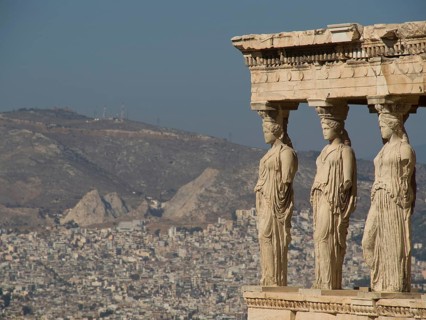 Ancient caryatid sculptures overlooking a city and mountain landscape, ancient columns against a