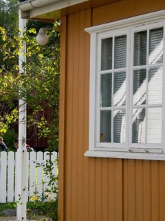 Close-up of a house with white windows next to a white fence, colourful wooden houses behind white