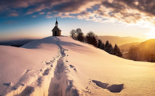 Footprints in fresh snow on a hill to a small chapel backlit in winter, AI generated, AI generated