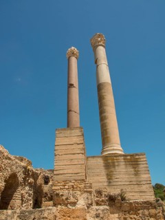 Two tall ancient columns rise into the blue sky, surrounded by ancient ruins, Tunis in Africa with