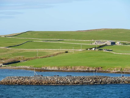 Small harbour landscape with green hills, houses and a stone embankment along the coast under a
