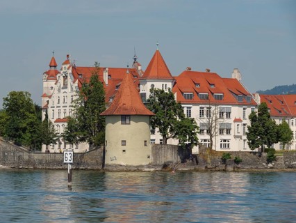 A castle with a red roof on the shore of a lake, a tower and dense trees, sky in the background,