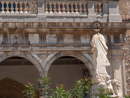 Marble sculpture of a figure and two angels in front of a church with arches and ornate details,