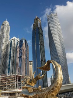 View of modern skyscrapers with a golden mermaid statue in the foreground and a clear blue sky,