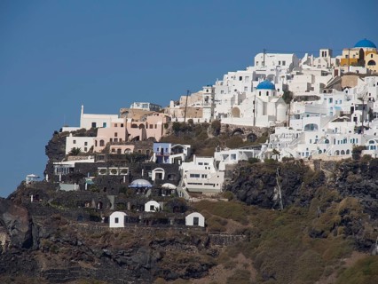 View of white buildings with blue domes on a cliff under a clear blue sky, The volcanic island of
