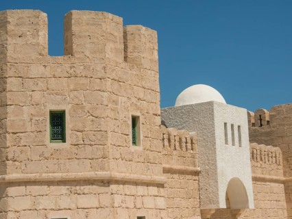 Sand-coloured fortress with green-framed windows and white dome under a blue sky, Tunis in Africa