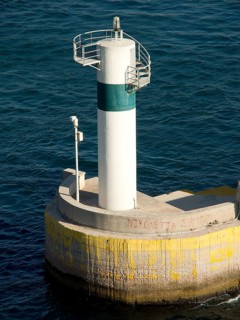 White-green lighthouse in the sea on a concrete base, Ancient building with columns and trees on