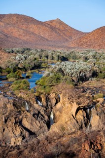 Kunene River with green vegetation in dry red mountain landscape, waterfall and African Baobab