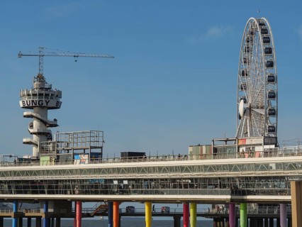 A leisure area with a large Ferris wheel and a bungee jumping tower on a colourful pier on the blue