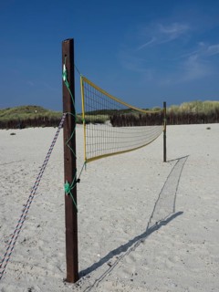 A volleyball net is set up in the sand on the beach, surrounded by dunes and grass, Heligoland,